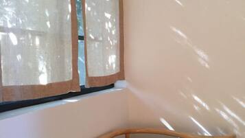 A corner of a room with a wooden chair, a window with sheer curtains, and a plain wall.