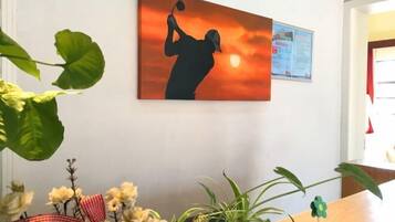 Una habitación con un cuadro que muestra una silueta contra un atardecer, una pizarra de anuncios y una mesa con plantas.