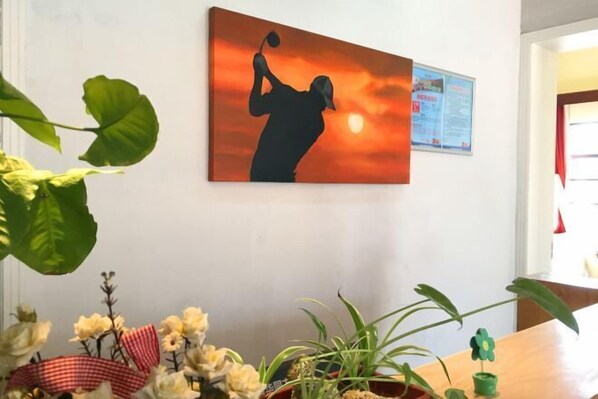 Una habitación con un cuadro que muestra una silueta contra un atardecer, una pizarra de anuncios y una mesa con plantas.