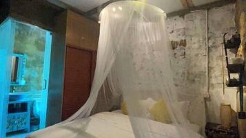 A room with a bed under a canopy, a wooden door, and a wall-mounted shelf with items.