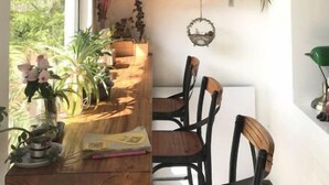 Una habitación con una mesa de comedor de madera, sillas, una lámpara colgante y estanterías con libros y plantas.