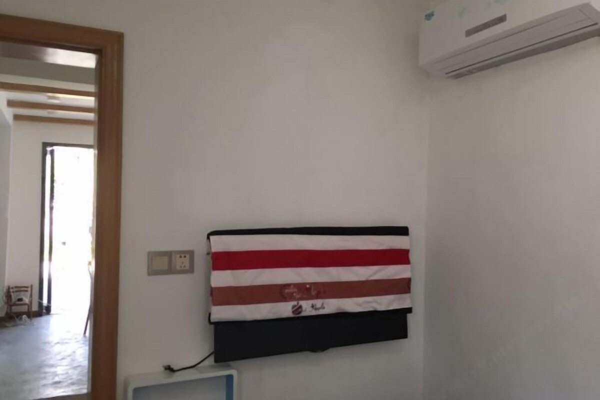 Una habitación con una bandera en la pared, un equipo de aire acondicionado y una puerta que da a otra habitación.