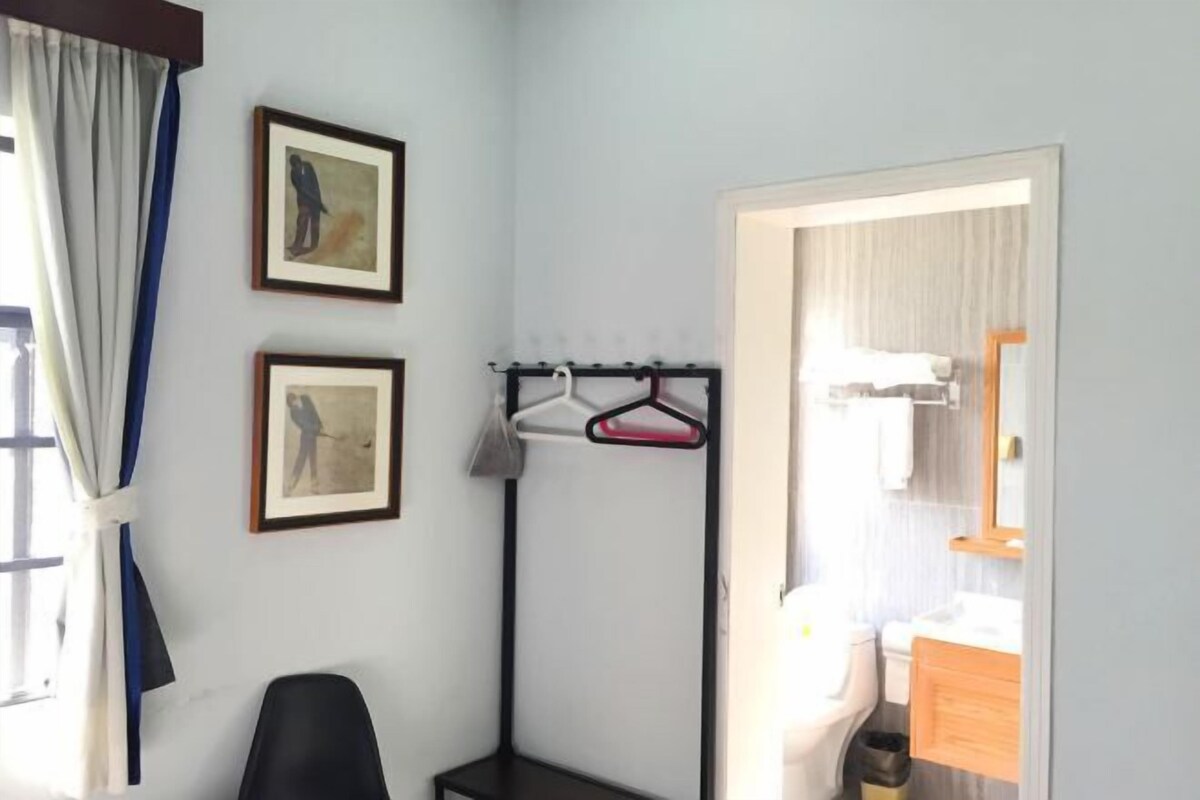 Habitación de hotel con cama, una silla, perchero y dos cuadros en la pared.