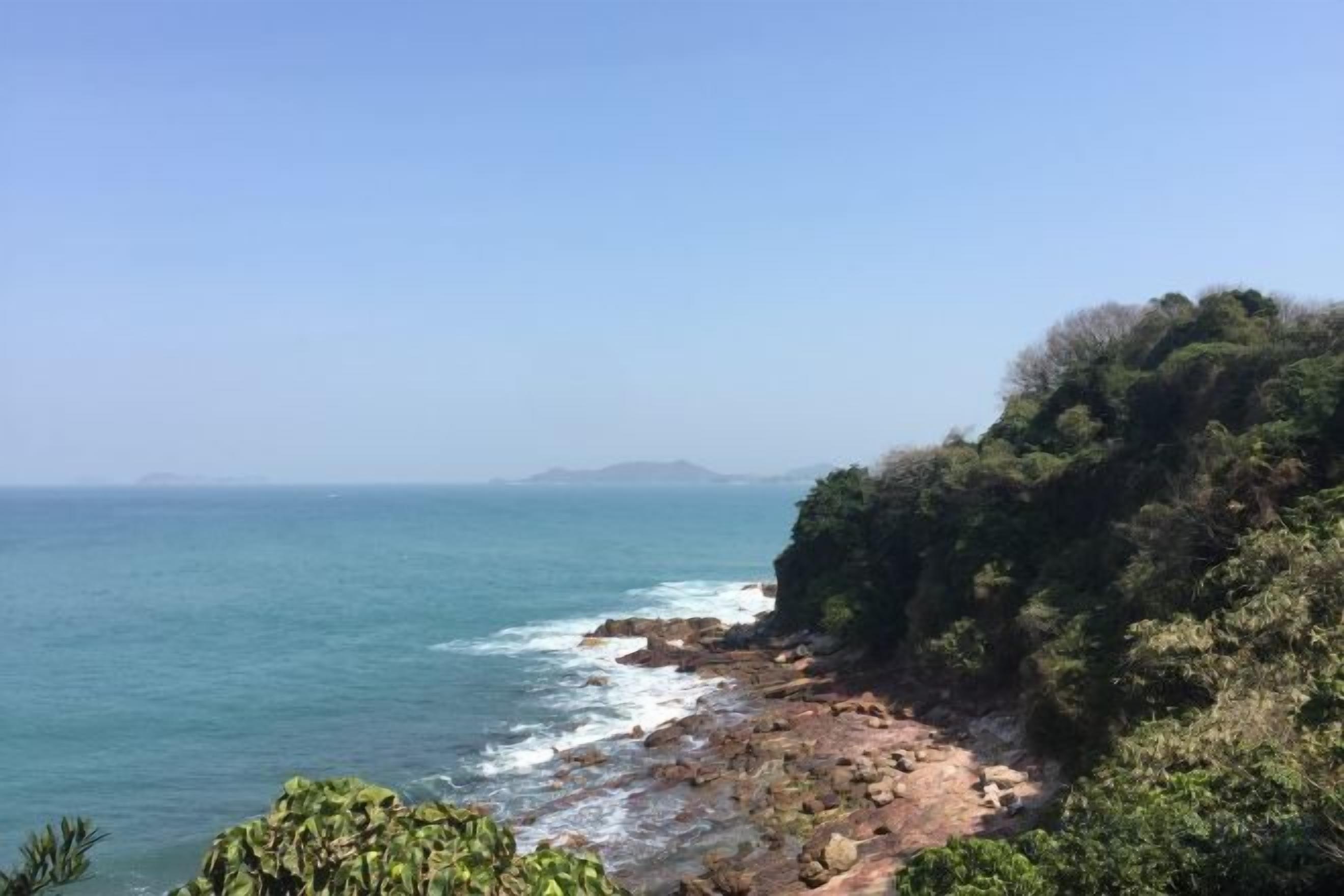 A coastal landscape with rocky terrain and dense vegetation.