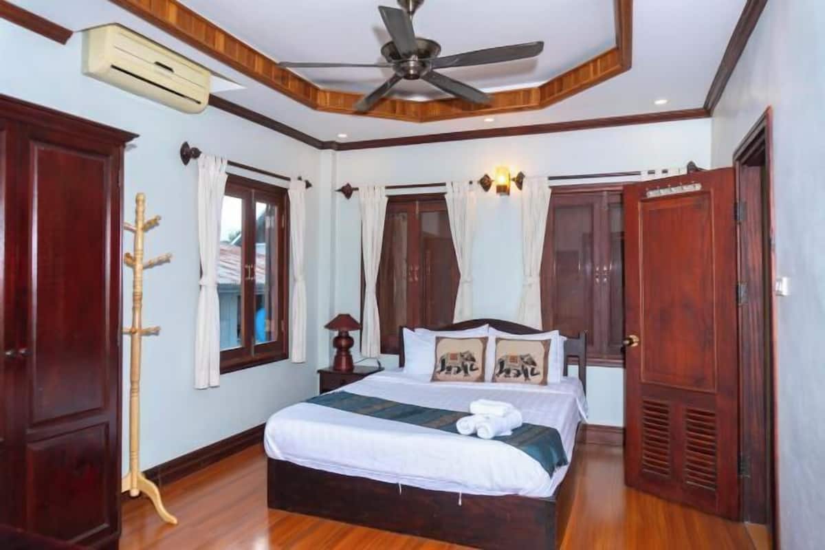 A bedroom with a wooden ceiling, a bed with white bedding, a ceiling fan, and a window with curtains.