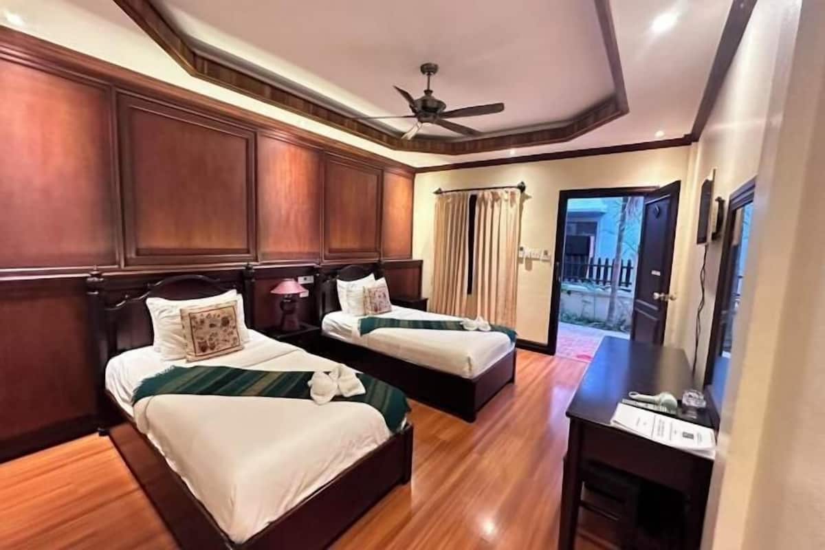 A hotel room with two beds, wooden paneling, a ceiling fan, and a desk with a chair.