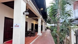 A covered outdoor corridor with a tiled floor, white columns, and a potted plant. - Y Not Lao Villa (Luang Prabang)