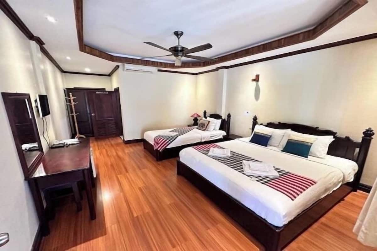 A hotel room with two beds, a desk, a ceiling fan, and a wooden floor.
