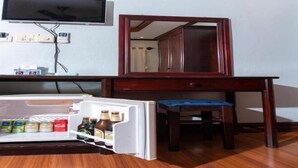 A compact room with a wooden desk, a television mounted on the wall, and a small refrigerator with beverages. - Y Not Lao Villa (Luang Prabang)