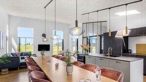 A modern kitchen with a central island, pendant lighting, and a large dining area with a long table and chairs. - Beautiful home in Børkop with sauna (Børkop)