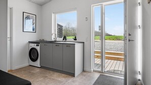 A modern kitchen with grey cabinets, a washing machine, and a window overlooking a garden. - Beautiful home in Børkop with sauna (Børkop)
