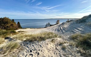 En sandstrand med fodspor, en klar himmel og havudsigt i det fjerne.