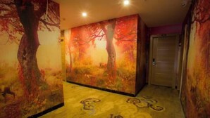 Un pasillo con un gran mural de árboles otoñales, una alfombra estampada y una puerta al final.