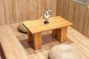 Una mesa de madera con una planta pequeña encima, sobre un suelo de madera y un tapete tejido cerca.