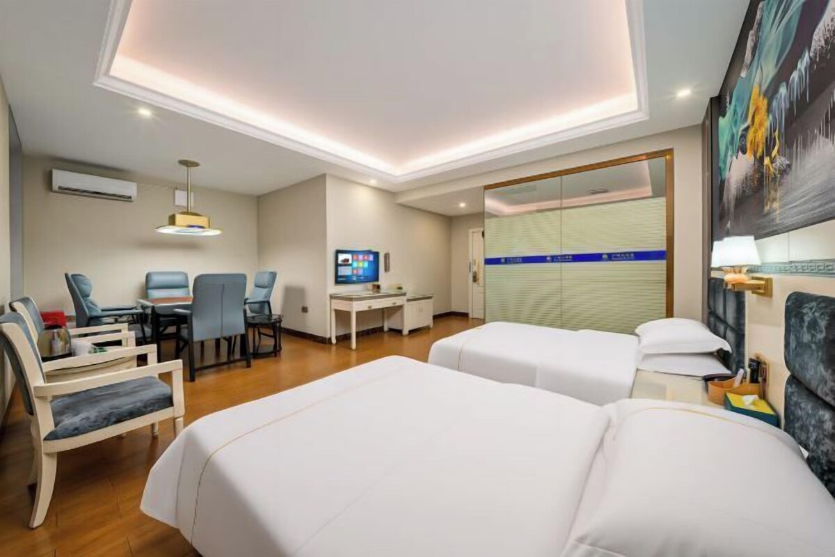 Habitación de hotel con dos camas, un escritorio con computadora, televisor y una zona de estar con sillas.