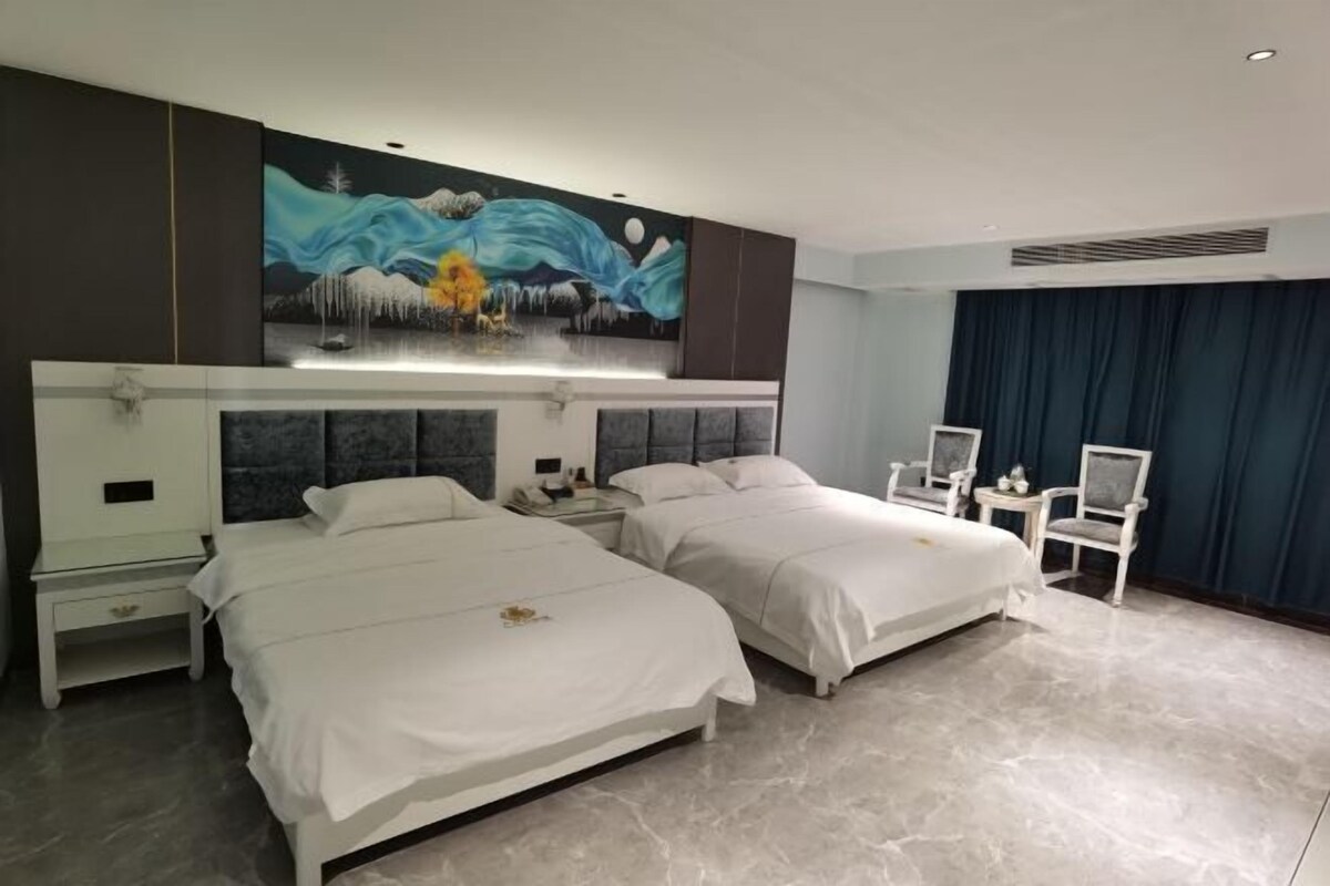 A hotel room with two beds, a large painting on the wall, a desk, and a chair.