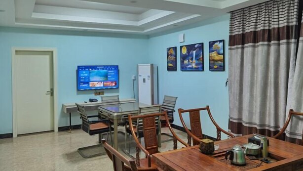 Un comedor con una mesa y sillas de madera, un televisor en la pared y una puerta a la izquierda.