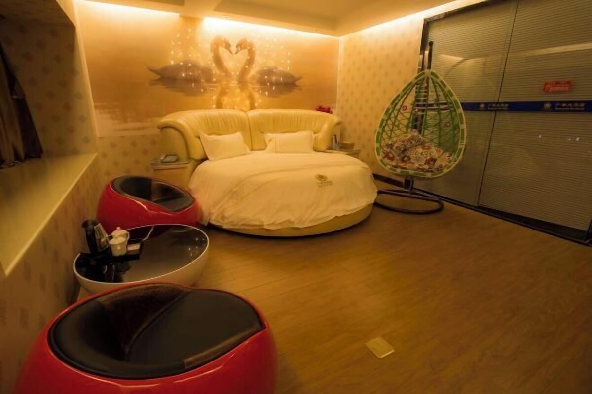 A hotel room with a bed, a red chair, a small table, and a hanging chair.