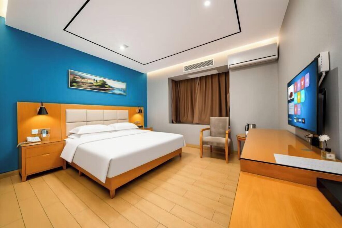 Habitación de hotel con cama, mesitas de noche, escritorio, silla, televisor y ventana con cortinas.