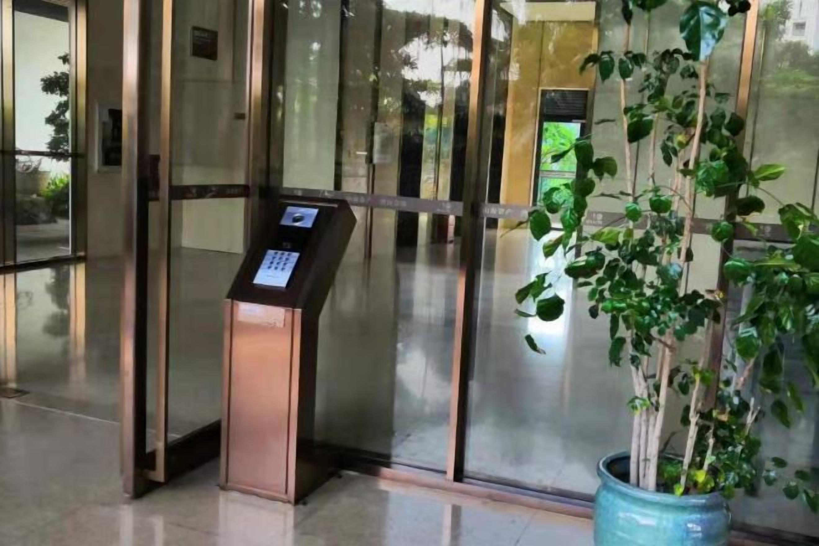En glasklagedør med et digitalt kioskanlæg og en potteplante ved siden af.