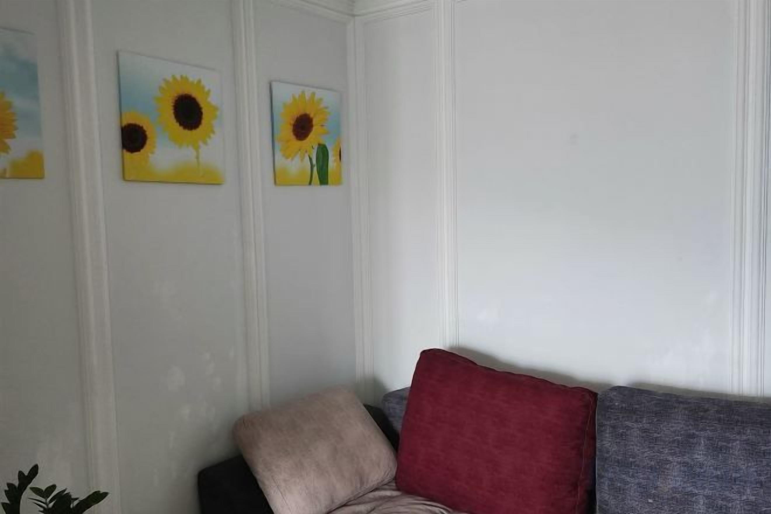 A room with a grey sofa, a red cushion, and three sunflower paintings on the wall.