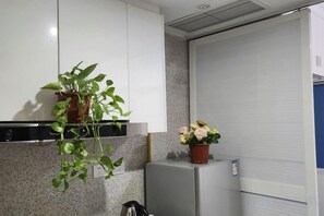 Una cocina con armarios blancos, un refrigerador, una planta en maceta y un arreglo floral.