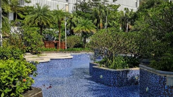 A swimming pool with tiled edges, surrounded by greenery and a building in the background.