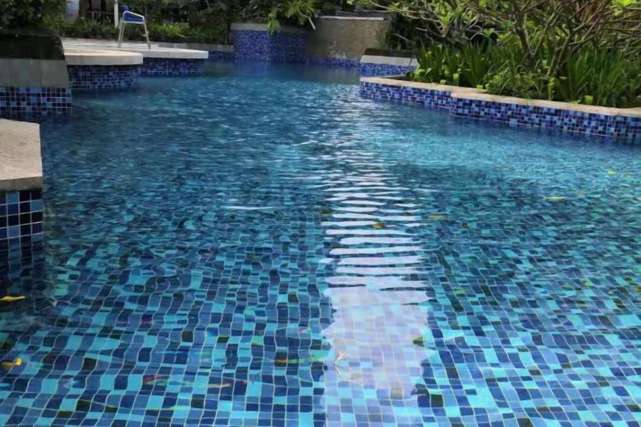 Une piscine dont le bord est revêtu de carreaux et dont l’eau est d’un bleu limpide.