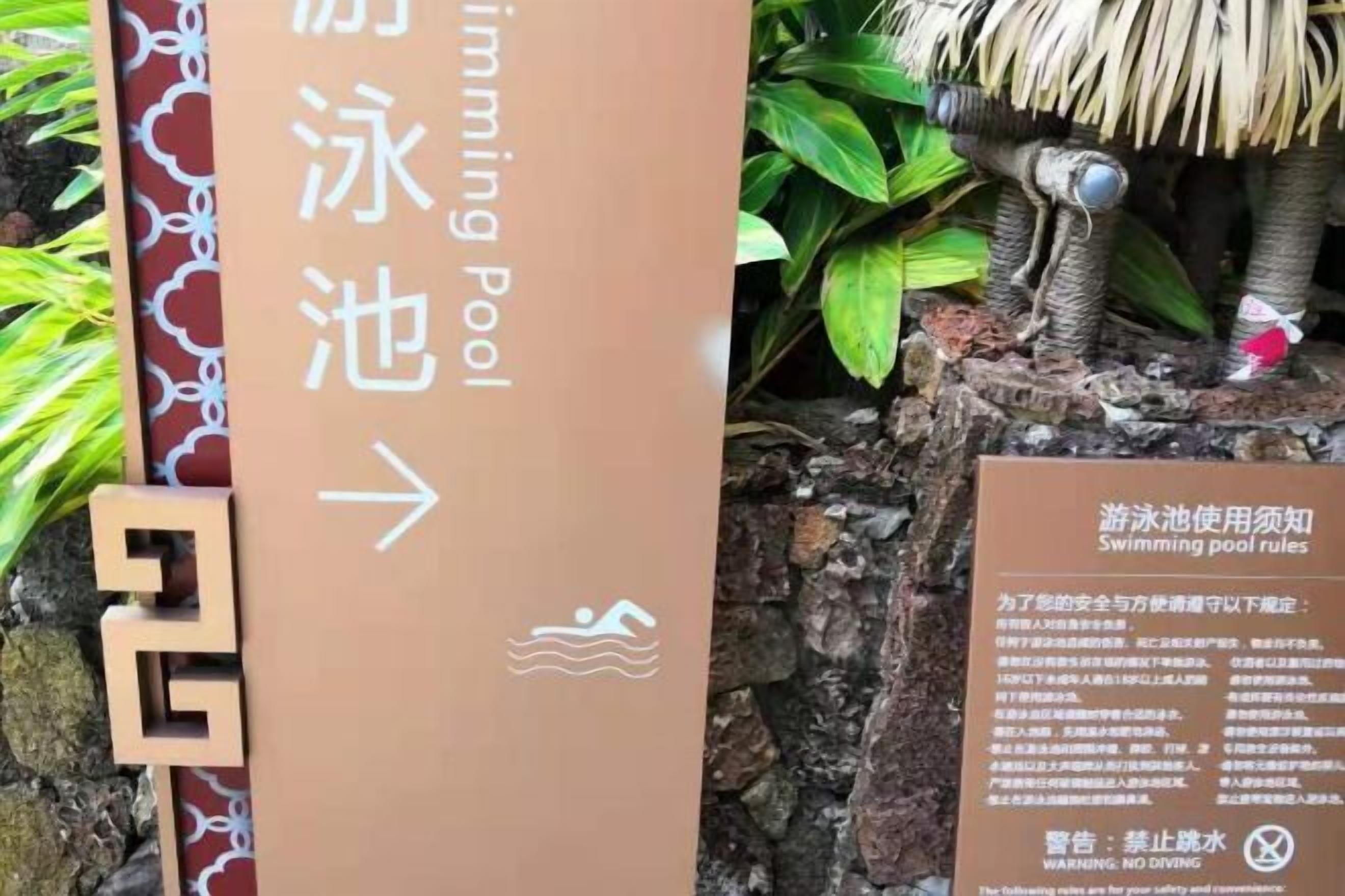 A directional sign for a swimming pool with a safety notice board beside it.