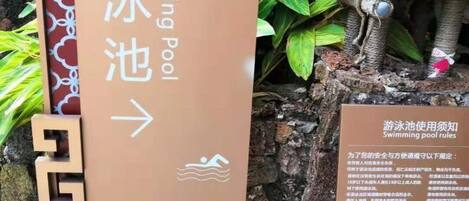 A directional sign for a swimming pool with a safety notice board beside it.