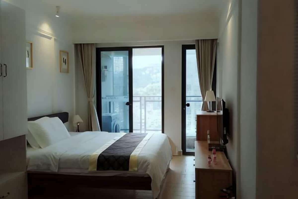 Habitación de hotel con cama, escritorio, silla, lámpara y balcón con vistas.