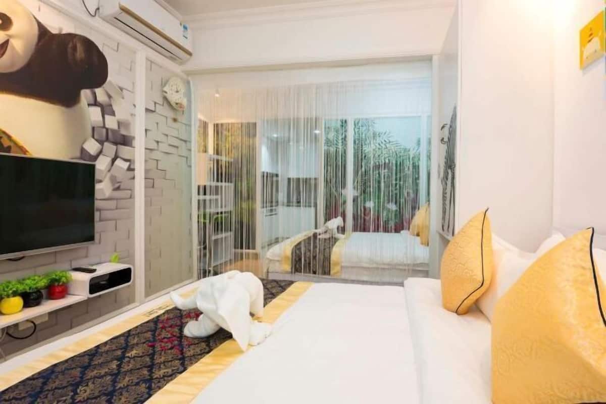 Habitación de hotel con cama, televisión, sofá y una gran decoración de panda.