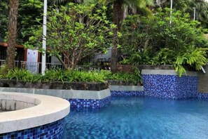 Una piscina con borde de azulejos, rodeada de vegetación y árboles.
