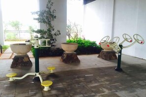 Buitenfitnessapparatuur, waaronder een hometrainer en een roeimachine, met op de achtergrond potplanten en een gebouw.