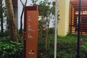 A directional sign with arrows pointing to different areas, surrounded by greenery and a building in the background. - Sweetome Vacation Rentals (Dapeng Banshanhai) (Shenzhen)