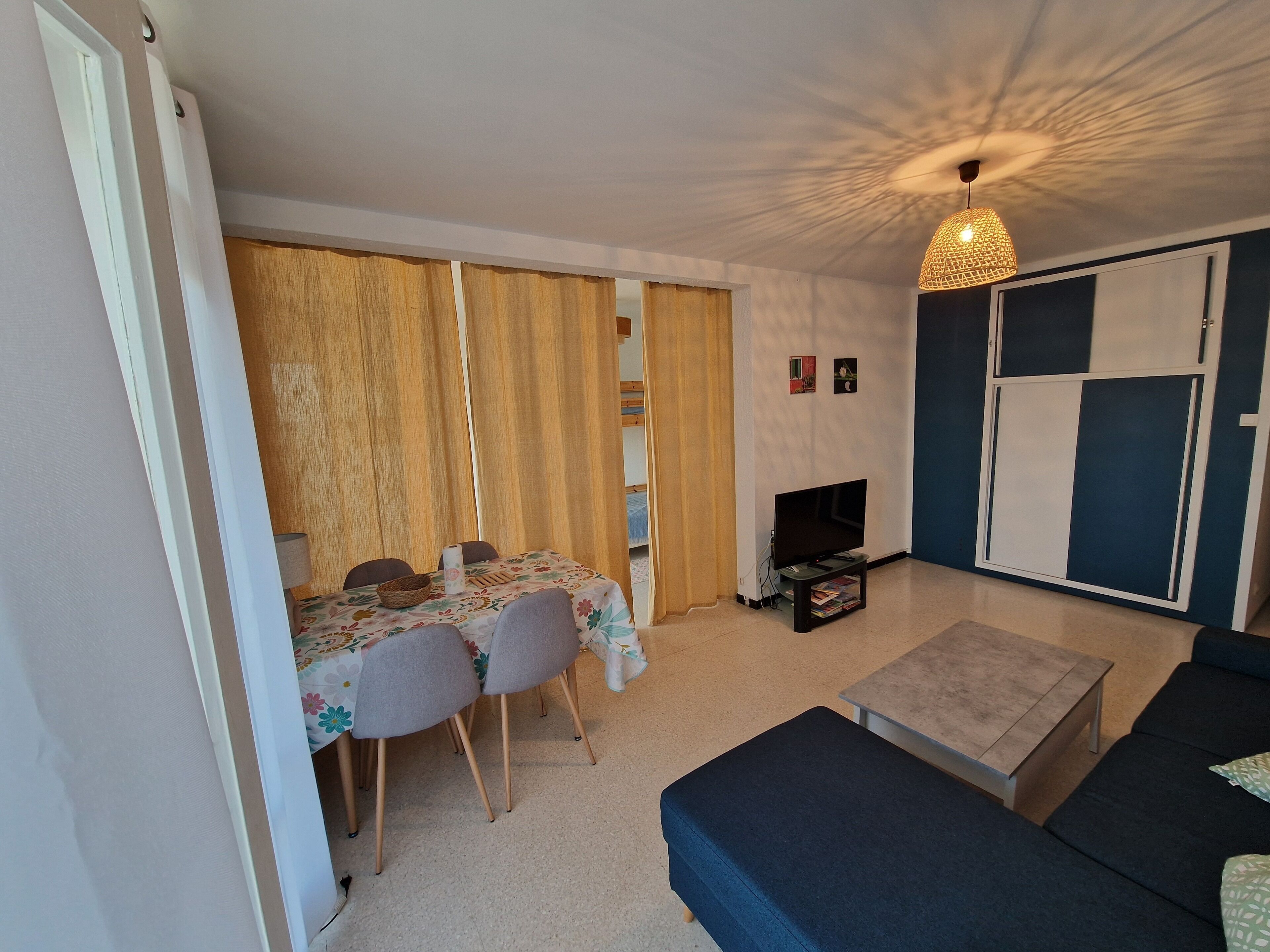 Een woonkamer met een bank, een televisie, een eettafel met stoelen en een schuifdeur.