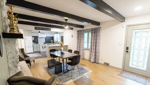 Un comedor moderno con una mesa y sillas de madera, una cocina al fondo y una planta decorativa en la pared.