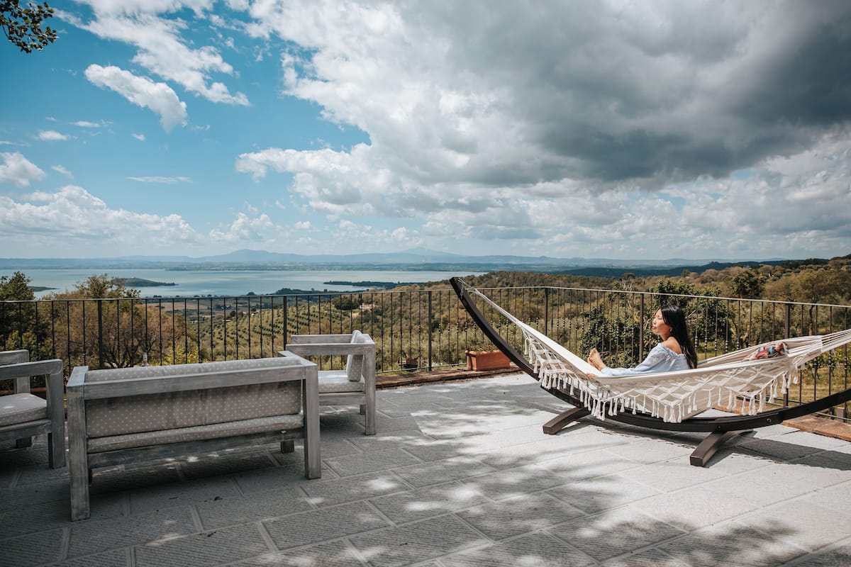 A hammock on a terrace overlooking a scenic landscape with a bench and a potted plant.