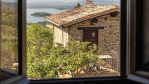 Ein Steinhaus mit Ziegeldach, einer Holztür und Blick auf einen See sowie Berge durch ein Fenster.