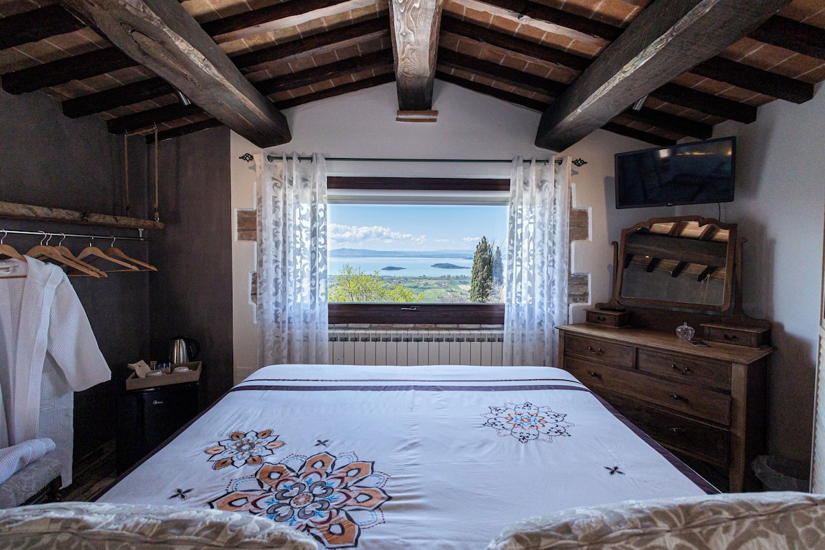 A bedroom with a large bed, a wooden dresser, a television, and a window with a view of the landscape.