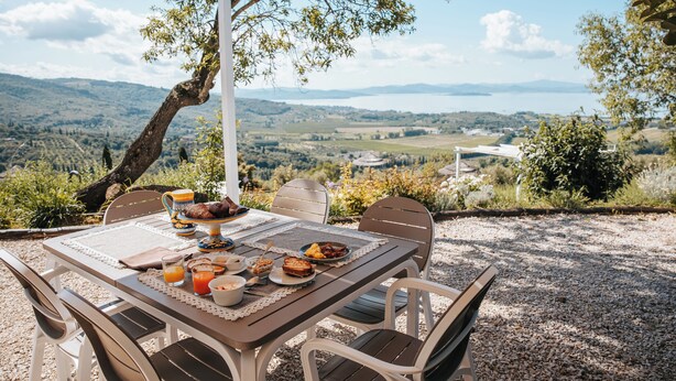 Ein Essbereich im Freien mit einem für das Frühstück gedeckten Tisch, mit Blick auf eine schöne Landschaft.