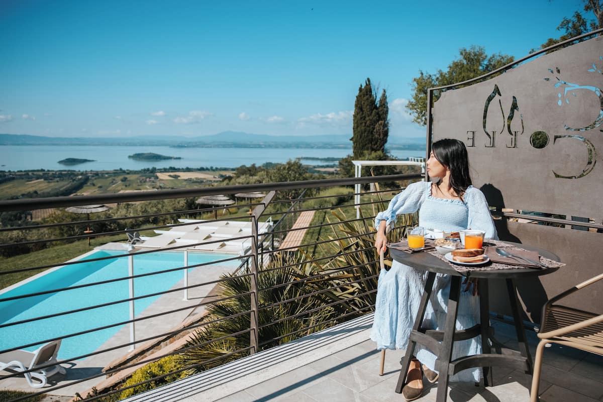 A woman sitting at a table with a view of a swimming pool and distant landscape.