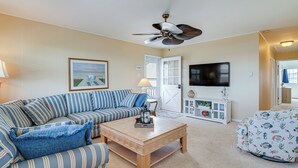 A living room with a striped sofa, a wooden coffee table, a ceiling fan, a television, and a patterned ottoman. - Walk to Beach: Ocean City Home w/ Deck & Views! (Ocean City)