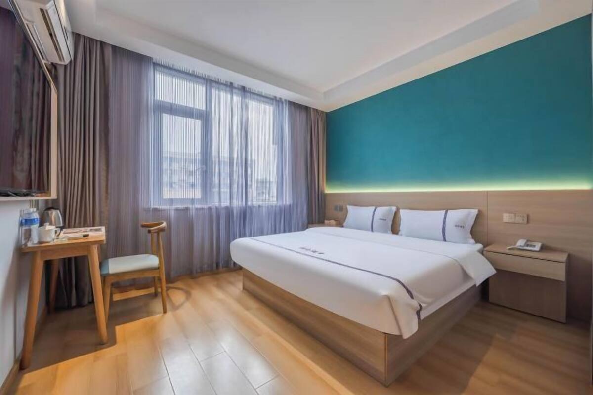Una habitación de hotel con cama, escritorio, silla, mesita de noche y ventana con cortinas.