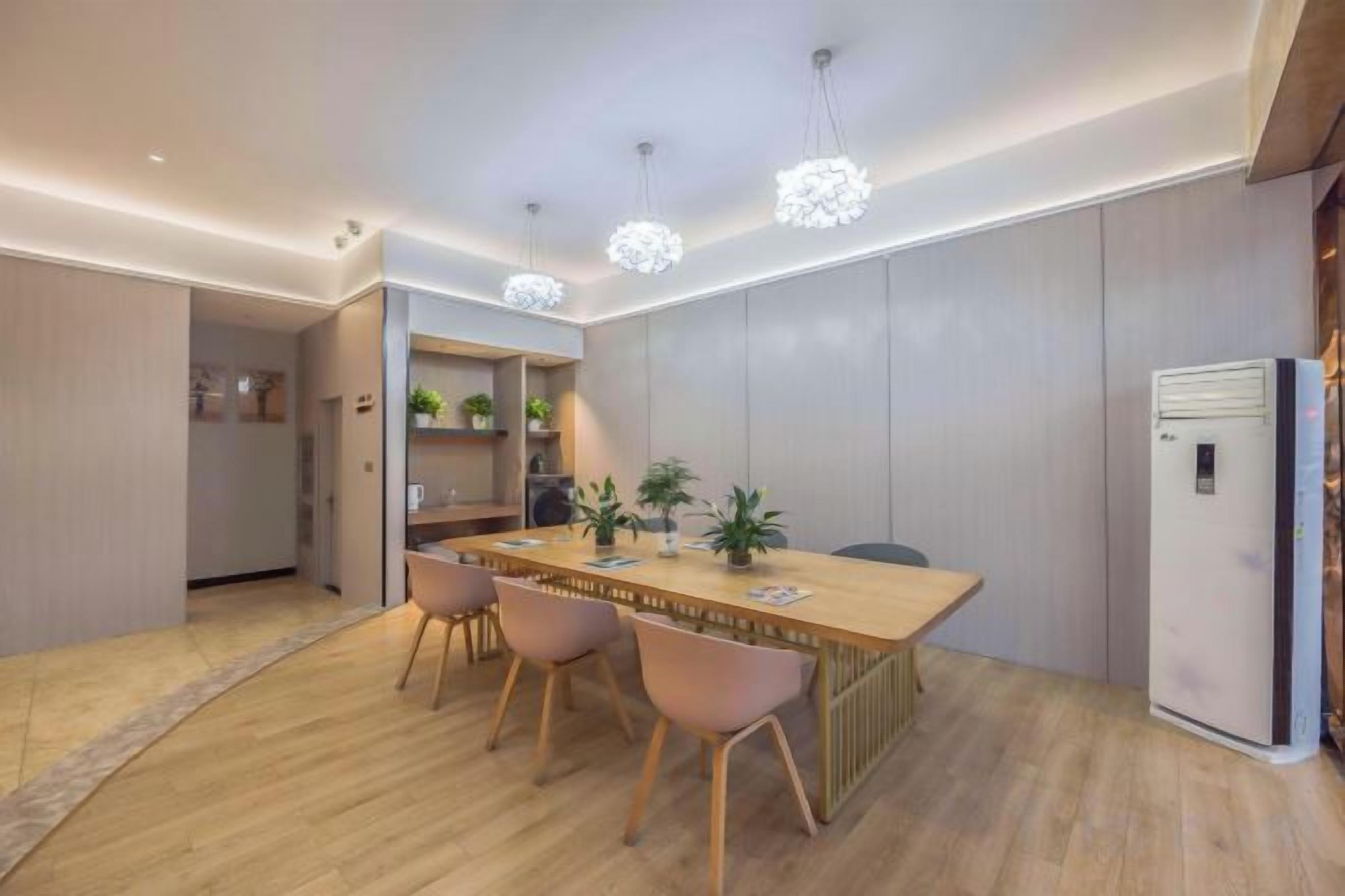 A modern dining area with a wooden table, chairs, pendant lighting, and a refrigerator.
