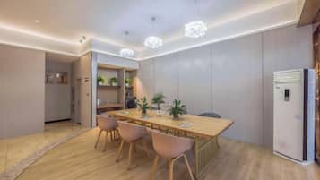A modern dining area with a wooden table, chairs, pendant lighting, and a refrigerator.