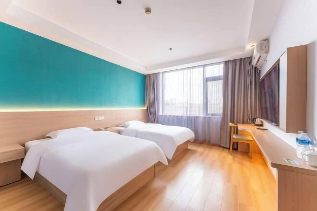 Habitación de hotel con dos camas, piso de madera, un ventanal con cortinas, un escritorio y un espejo.