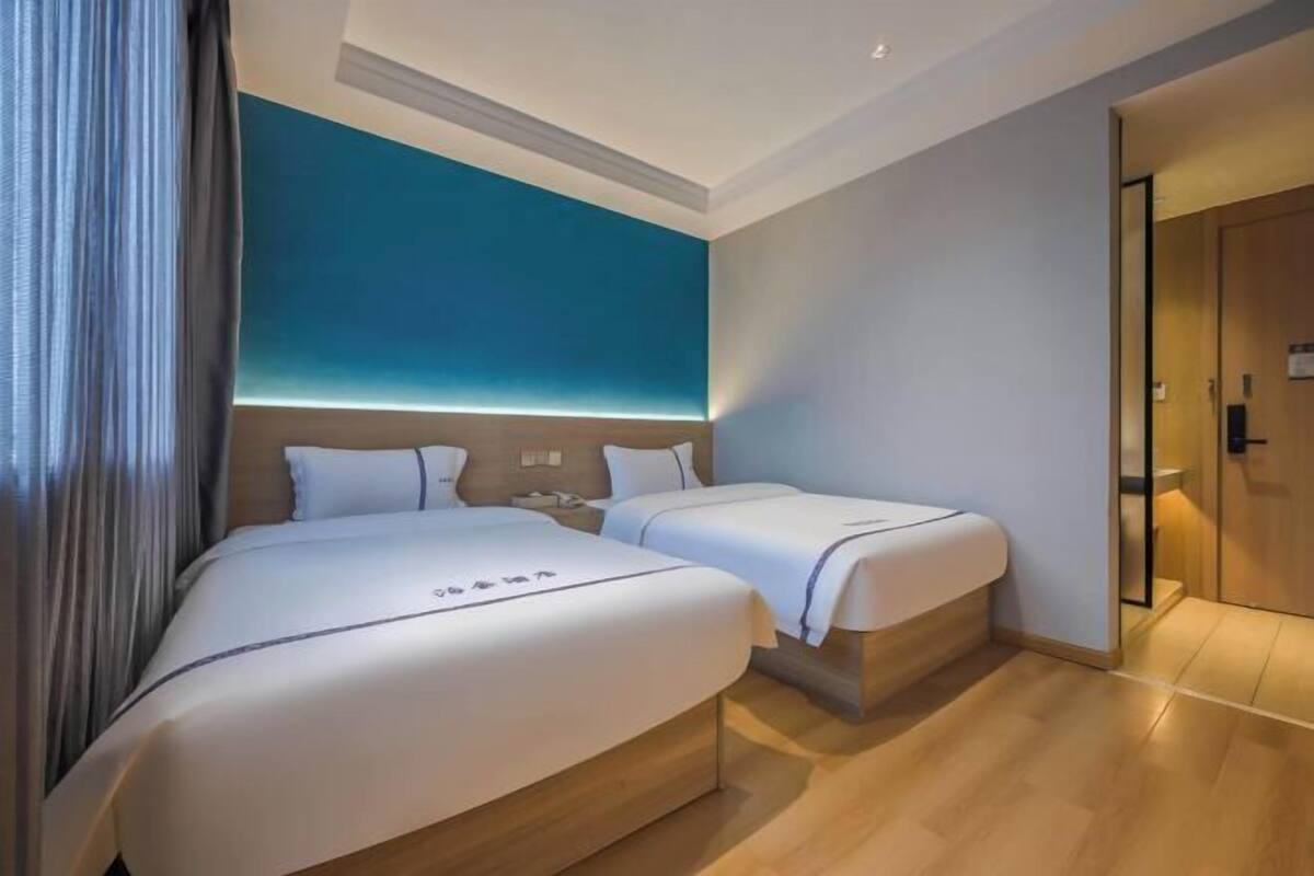 Habitación de hotel con dos camas, una pared de acento azul, suelo de madera y una puerta a la derecha.