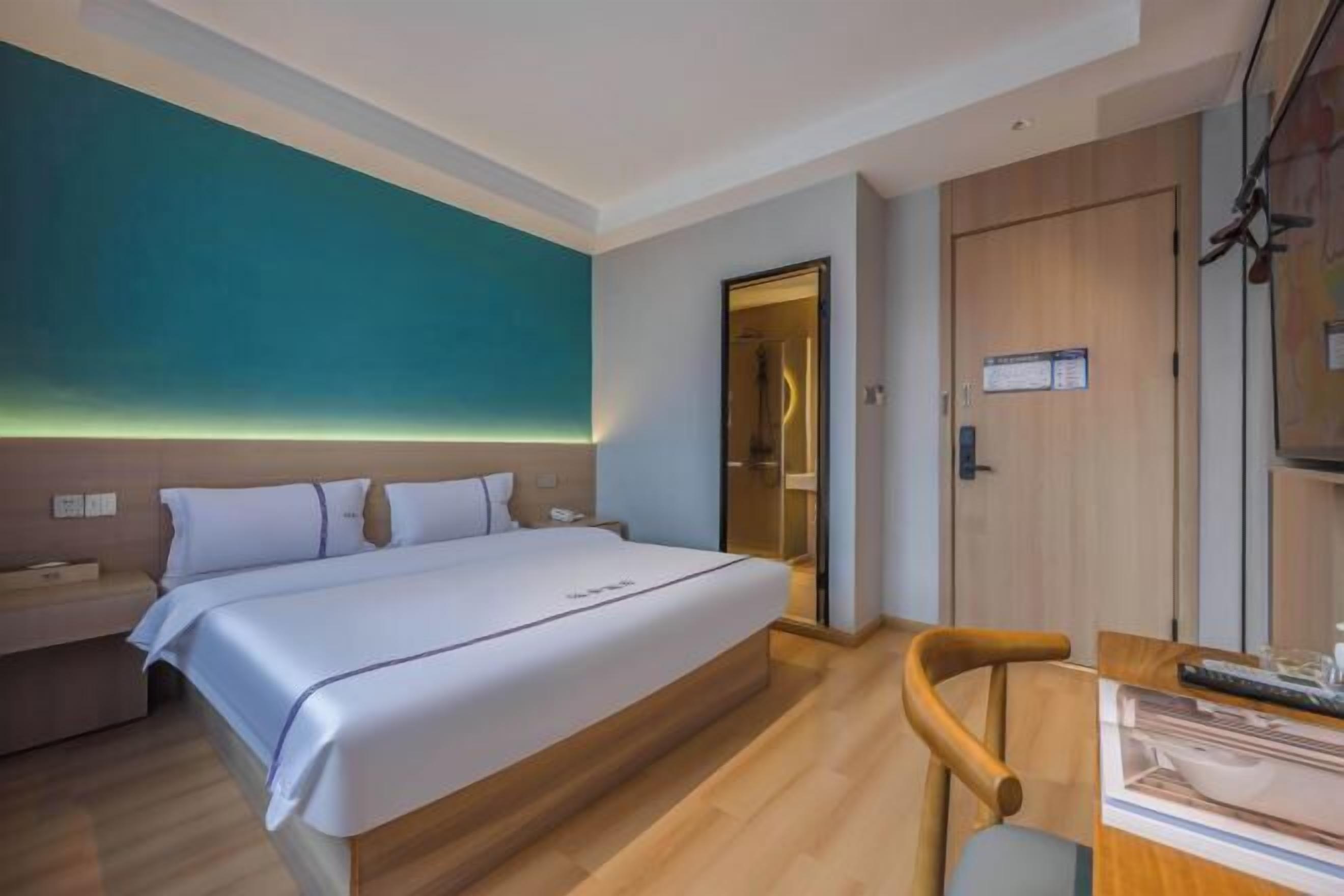 A hotel room with a bed, bedside table, and a desk with a chair.