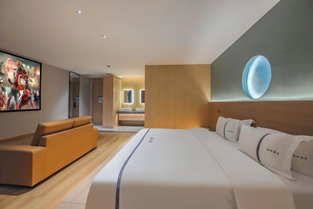 A modern hotel room with a large bed, a sofa, a painting, and a unique wall feature.